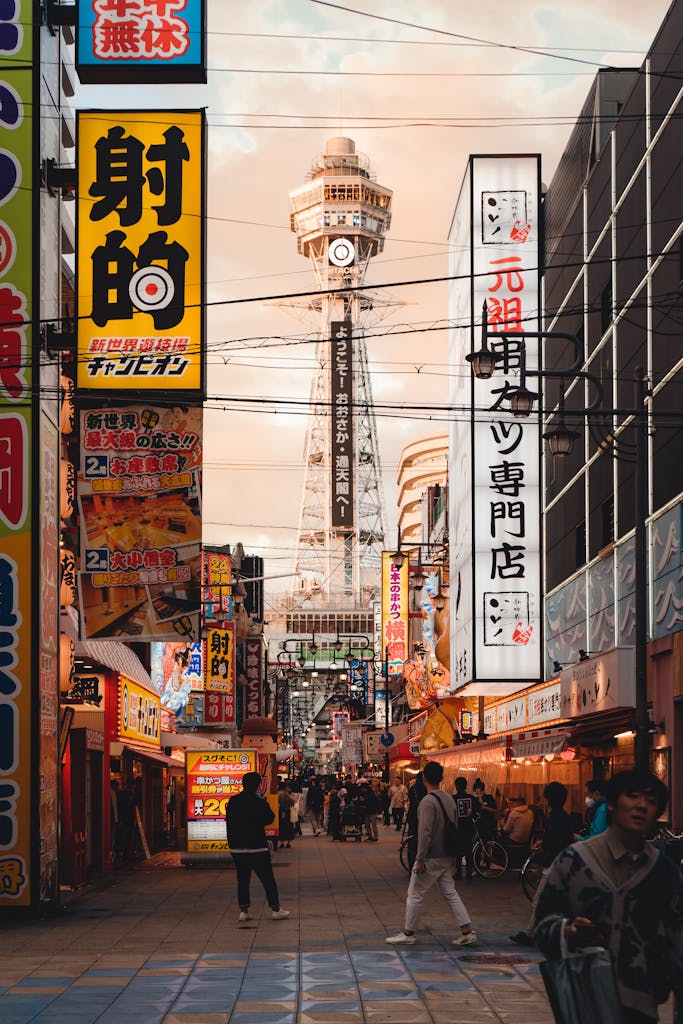 Lively street scene in Osaka featuring Tsutenkaku Tower with vibrant signs and bustling crowds.
