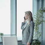 A professional businesswoman talking on the phone in a modern office setting with natural light.
